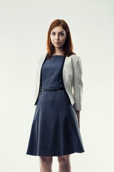 Woman with auburn hair, dressed in a white blazer and dark dress, stands confidently. Her poised demeanor and professional attire highlight her competence and authority