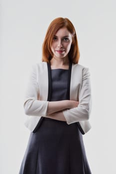 Woman with auburn hair, wearing a white blazer over a dark dress, crosses her arms with confidence. Her professional appearance suggests a role in business or leadership