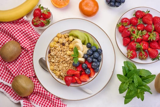 Granola with strawberries, kiwi, banana and blueberries in a round plate on a white table. Healthy and tasty food, top view
