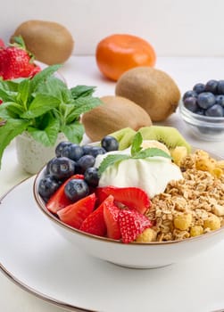 Granola with strawberries, kiwi, banana and blueberries in a round plate on a white table. Healthy and tasty food, top view