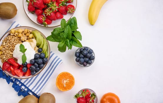 Granola with strawberries, kiwi, banana and blueberries in a round plate on a white table. Healthy and tasty food, copy space
