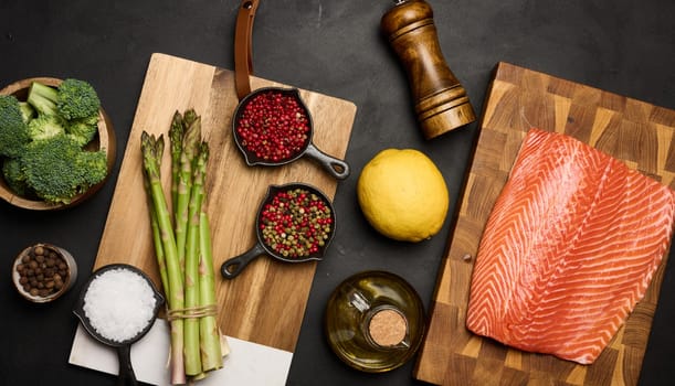 A piece of raw trout fillet on a wooden board, next to asparagus and broccoli. View from above