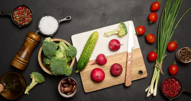 Green lettuce, broccoli, radishes and tomatoes on a black table. Salad ingredients