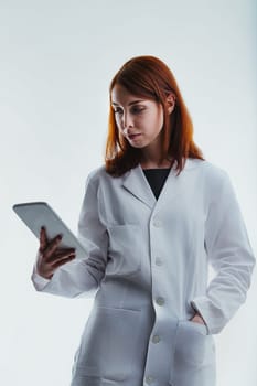 red-haired scientist in a white lab coat examines a tablet thoughtfully. Her professional demeanor reflects her role as a specialized technician and researcher, focused on scientific exploration