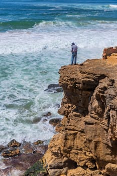 Sintra, Portugal: April 13, 2024: A fisherman stands on the edge of a cliff by the ocean in Ericeira, Portugal