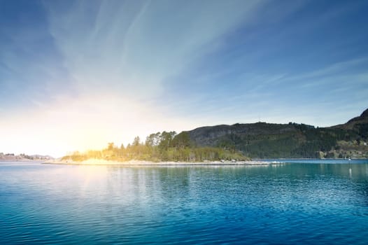 Island with rocks and trees in the fjord in front of the open sea in Norway. The water glistens in the sun. Landscape from the north