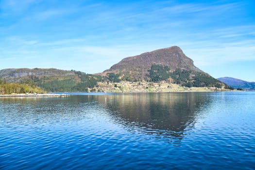 Norwegian fjord landscape. View of mountains with rugged vegetation. Crystal clear water in the foreground. Landscape from Scandinavia