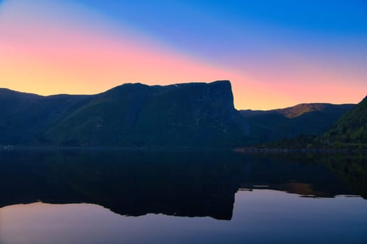 Norwegian fjord landscape at dusk. View of mountains with rough vegetation. Crystal clear water in the foreground. Landscape from Scandinavia