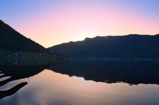 Norwegian fjord landscape at dusk. View of mountains with rough vegetation. Crystal clear water in the foreground. Landscape from Scandinavia