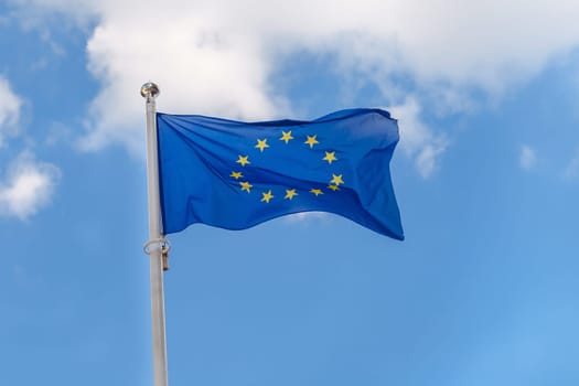 Close-up the flag of the EU (European Union) flies against the background of a cloudy blue sky