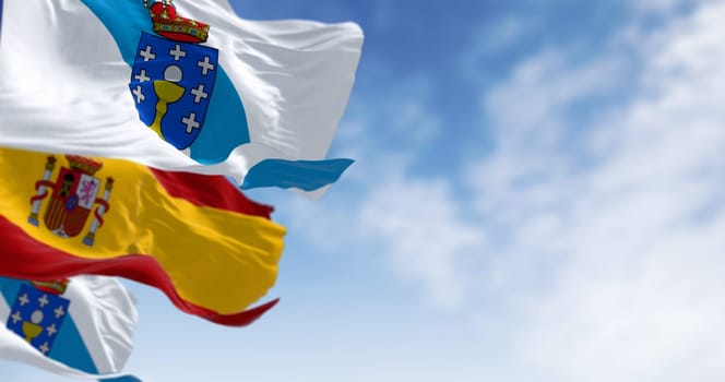 Flags of Galicia and Spain waving on a clear day. Autonomous community of Spain. White with a blue diagonal band with coat of arms on top. 3d illustration render. Selective focus. Fluttering fabric