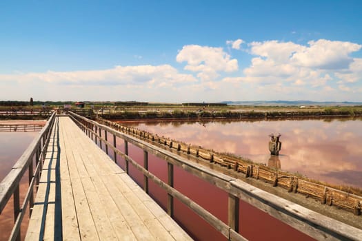 Board walk into the Burgas Salt Pans, a group of salty pools at Atanasovsko, Atanasovo Lake, the sky and its clouds are reflecting perfectly in the smooth surface of the pink water, Burgas, Bourgas, Bulgaria 2022