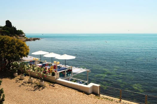 Beautiful view onto the deep blue sea from the old town of Nessebar, Nesebar with a restaurant terrace in the foreground with colorful chairs, table cloths and white umbrellas, Bulgaria 2022