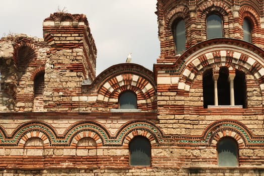 Seagull sitting on the roof above the beautiful facade of the Church of Christ Pantocrator in the old town of Nessebar, Nesebar, elaborate patterns out of bricks and colorful tiles around the windows, Bulgaria 2022