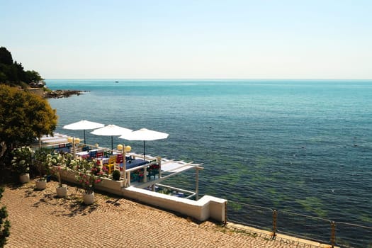 Picturesque view onto the deep blue sea from the old town of Nessebar, Nesebar with a restaurant terrace in the foreground with colorful chairs, table cloths and white umbrellas, Bulgaria 2022