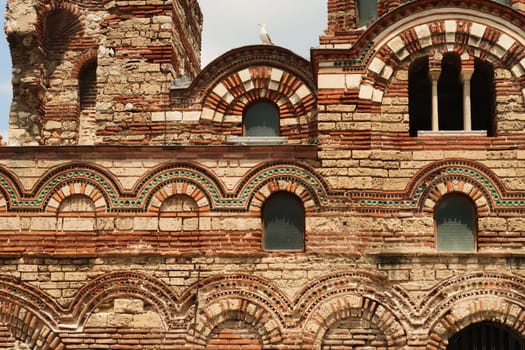Seagull sitting on the roof above the facade of the Church of Christ Pantocrator in the old town of Nessebar, Nesebar, elaborate patterns out of bricks and colorful tiles around the windows, Bulgaria 2022