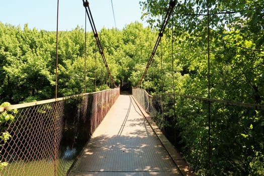 The Mavrikov Rope Bridge, a small metal pedestrian suspension bridge over the Yantra River in a lush dense forest around Veliko Tarnovo, Bulgaria 2022