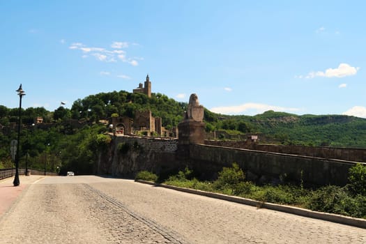 Cobble stone street next to the entrance gate of the Tsarevets Fortress, its walls and the hill with the Patriarchal Cathedral, Church of the Holy Ascension of the Lord can be seen in the background, Veliko Tarnovo, Bulgaria 2022