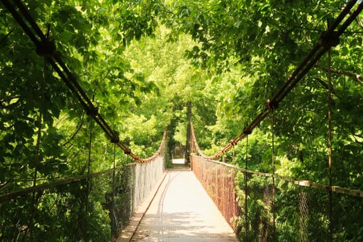 Walking over the Mavrikov Rope Bridge, a small metal pedestrian suspension bridge over the Yantra River surrounded by a lush and dense forest of an intense green color, Veliko Tarnovo, Bulgaria 2022