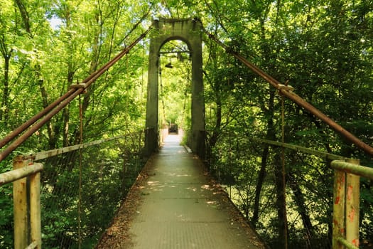 Entering the Mavrikov Rope Bridge, a small metal pedestrian suspension bridge over the Yantra River in a lush and dense forest around Veliko Tarnovo, Bulgaria 2022