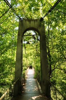 Entering the Mavrikov Rope Bridge, a small metal pedestrian suspension bridge over the Yantra River in the dense lush forest around Veliko Tarnovo, Bulgaria 2022