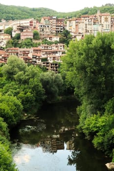 The old town of Veliko Tarnovo is reflecting in the water of the Yantra River, surrounded by dense and lush forest, Veliko Tarnovo, Bulgaria 2022