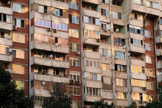 The sunset reflecting in the many windows of a concrete, socialist, brutalist panel, multi-story, high-rise, apartment block, building, orange, yellow, pink reflection, Sofia, Bulgaria 2022