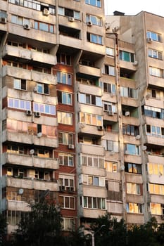 The sunset reflecting in orange, yellow, pink in the many windows of a concrete, socialist, brutalist panel, multi-story, high-rise, apartment block, building, Sofia, Bulgaria 2022