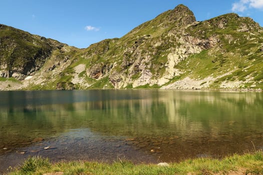 The mountains are reflecting on green, blue and turquoise water of the Kidney, Babreka Lake, one of the Seven Rila Lakes, situated on a plateau in the Rila National Park, close to Sofia, Bulgaria 2022