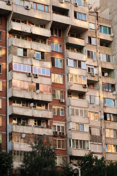 Orange, yellow, pink reflection of the sunset in the many windows of a concrete, socialist, brutalist panel, multi-story, high-rise, apartment block, building, Sofia, Bulgaria 2022