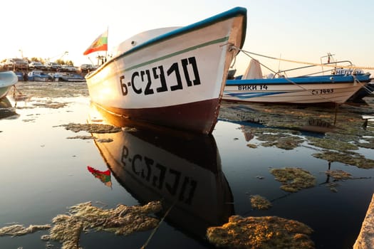 A fisherboat with the bulgarian flag perfectly reflecting in the water at the harbor, port next to the old town of Sozopol, Sosopol, Bulgaria, 4th of July 2022