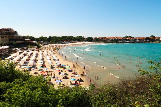 View onto the Sozopol Central Beach on a busy day, many white beach umbrellas and sun chairs on the beach, the intense turquoise blue sea and the old town of Sozopol, Sosopol in the background, Bulgaria, 5th of July 2022