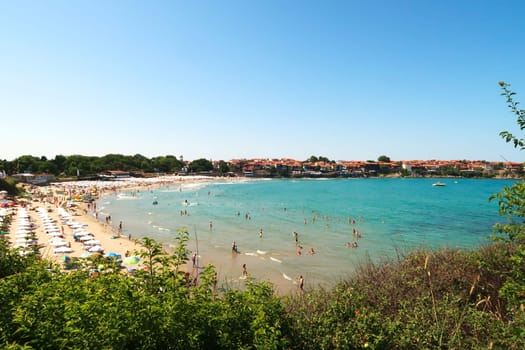 View onto the Sozopol Central Beach on a busy day, white beach umbrellas and sun chairs on the beach, the intense turquoise blue sea and the old town of Sozopol, Sosopol in the background, Bulgaria, 5th of July 2022