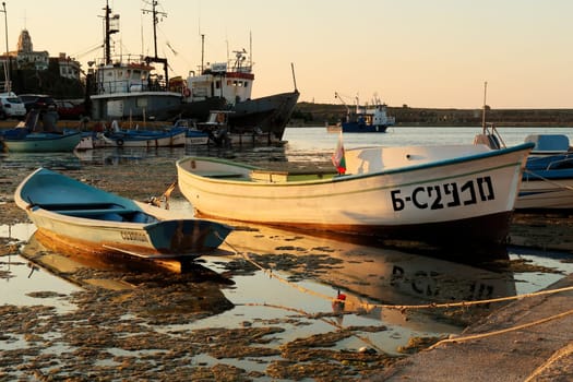 Small fisherboats reflecting in the water at the golden hour in the harbor, port next to the old town of Sozopol, Sosopol, Bulgaria, 4th of July 2022