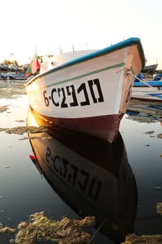A fisherboat with the bulgarian flag reflecting perfectly in the water at the harbor, port next to the old town of Sozopol, Sosopol, Bulgaria, 4th of July 2022