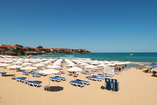The Sozopol Central Beach, many white beach umbrellas and sun chairs in the foreground and the sea and the old town of Sozopol, Sosopol in the background, Bulgaria, 5th of July 2022