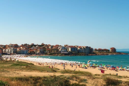 View onto Harmanite, Kharmanite on a busy day, many white beach umbrellas and sun chairs on the beach, the intense turquoise blue sea and the town of Sozopol, Sosopol in the background, Bulgaria, 5th of July 2022