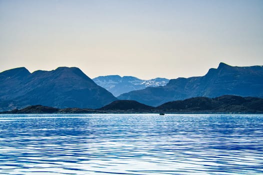Norwegian fjord landscape. View of snow-capped mountains with rugged vegetation. Crystal clear water in the foreground. Landscape from Scandinavia