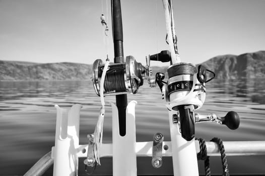 Fishing boat with fishing rod and fishing reels in front of mountains in the Norwegian fjord landscape in black and white. Crystal clear water in Scandinavia