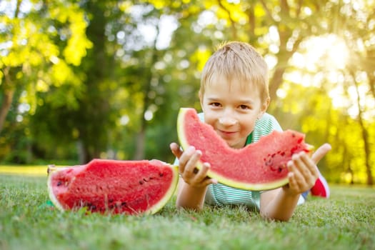 Cute child lying on the grass and eating juicy slice of watermelon. Family and relationship concept.