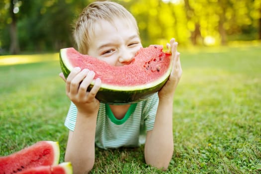 Cute child lying on the grass and eating juicy slice of watermelon. Family and relationship concept.