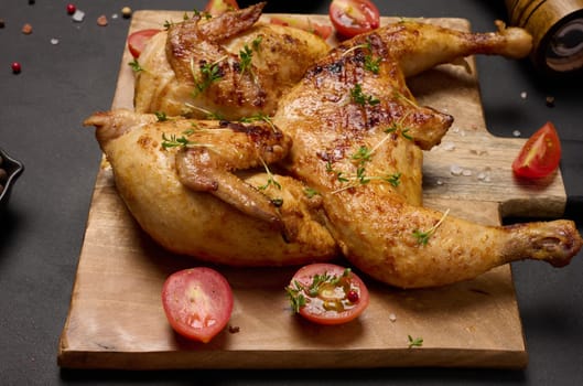 Whole fried chicken with spices on a wooden board on a black table, top view