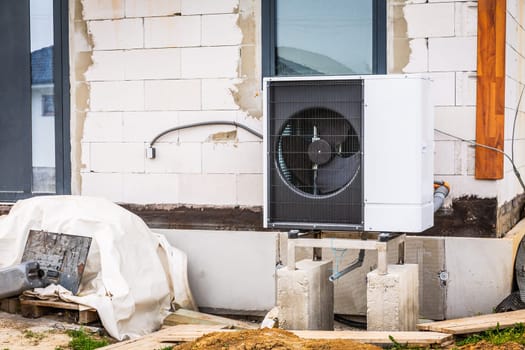 Air source heat pump installed outside of new and modern house under construction, green renewable energy concept of heat pump