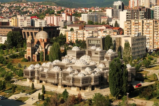 View from the bell, clock tower of the Cathedral of Saint, St. Mother Theresa onto the National University Library of Kosovo, an example of brutalist, socialist architecture in the city center of Prishtina, Pristina, Kosovo 2022
