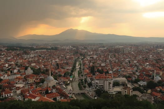 View from the Prizren Fortress onto the old town of Prizren before sunset, golden sunlight breaking through a cloudy sky, Prizren, Kosovo 2022