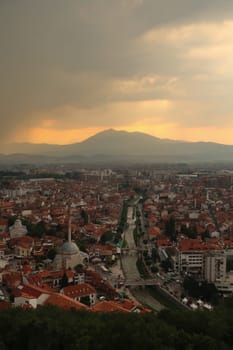 View from the Prizren Fortress onto the Bistrica River and the old town of Prizren before sunset, golden sunlight and a cloudy sky, Prizren, Kosovo 2022