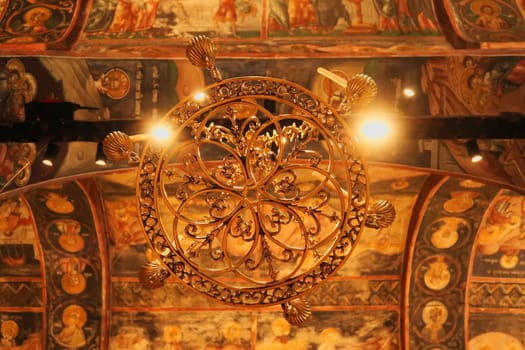 Chandelier inside the Church Complex of the Patriarchate of Pec Monastery, hanging from a ceiling completely covered in colorful paintings, frescos, outside of Peja, Kosovo 2022