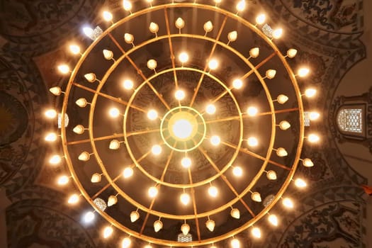 Looking up to the majestic chandelier hanging from the ceiling with elaborate painting, fresco, pattern decoration inside the Sinan Pasha Mosque, an ottoman mosque in the old town of Prizren, Kosovo 2022