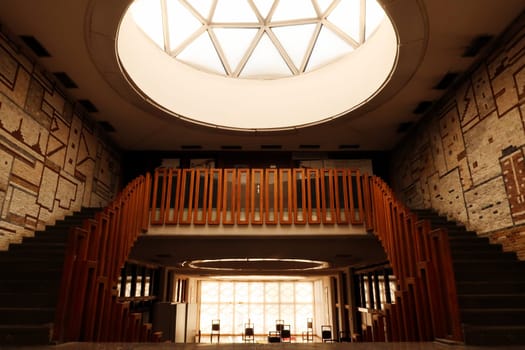 Light is shining throug a big dome with geometric pattern onto the stairs, staircase, hallway with wooden rails, handrails, railings inside the National University Library of Kosovo, Prishtina, Pristina, Kosovo, 25th of July 2022