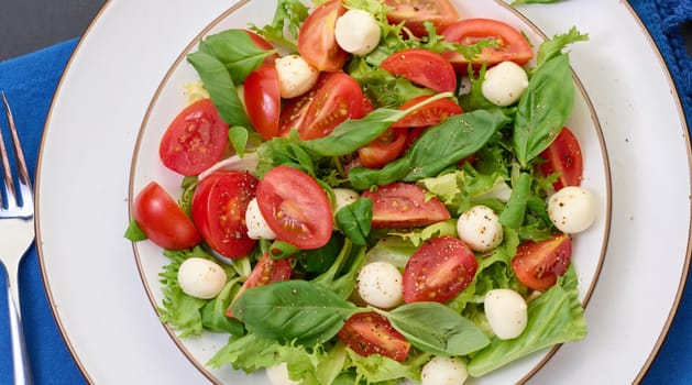 Salad with mozzarella, cherry tomatoes and green lettuce in a white round plate, top view